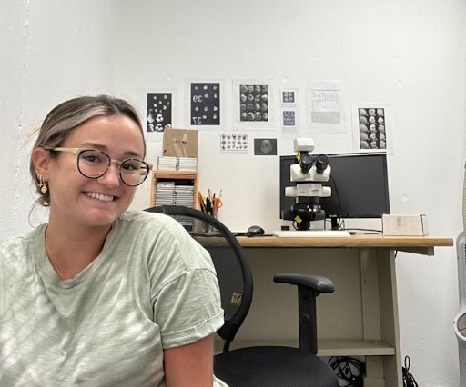ALT: Gabriella Lirio smiling, sitting in front of a desk that holds scientific tools 

