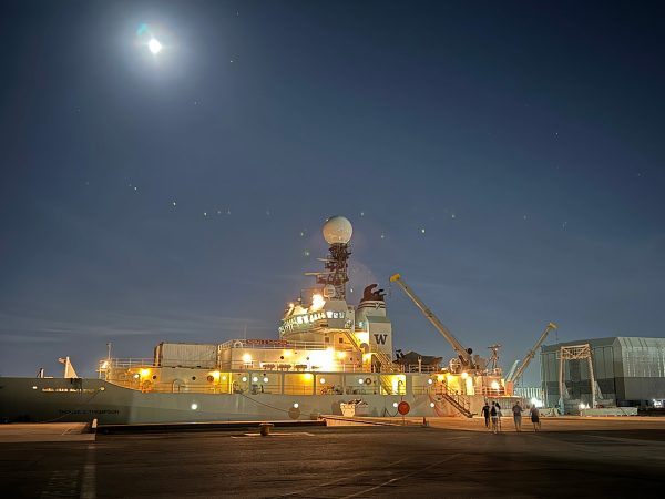 The R/V Thomas Thompson at the dock in Fremantle, Australia benath the night sky with the glimmer of the moonlight trickling from above and the yellow lights of the ship beaming like stars stolen from the darkness above