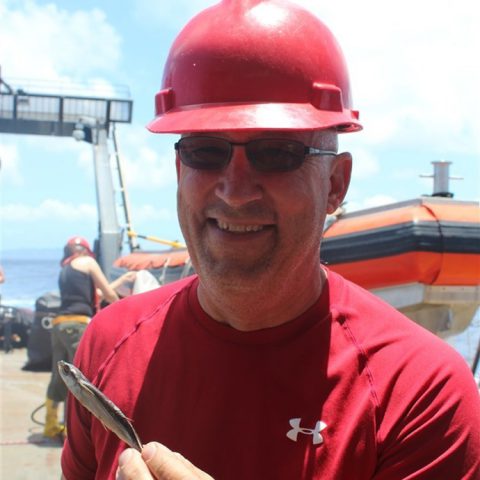 John Lamkin sostiene un pez volador que encontró su camino a bordo. Crédito de la imagen: NOAA