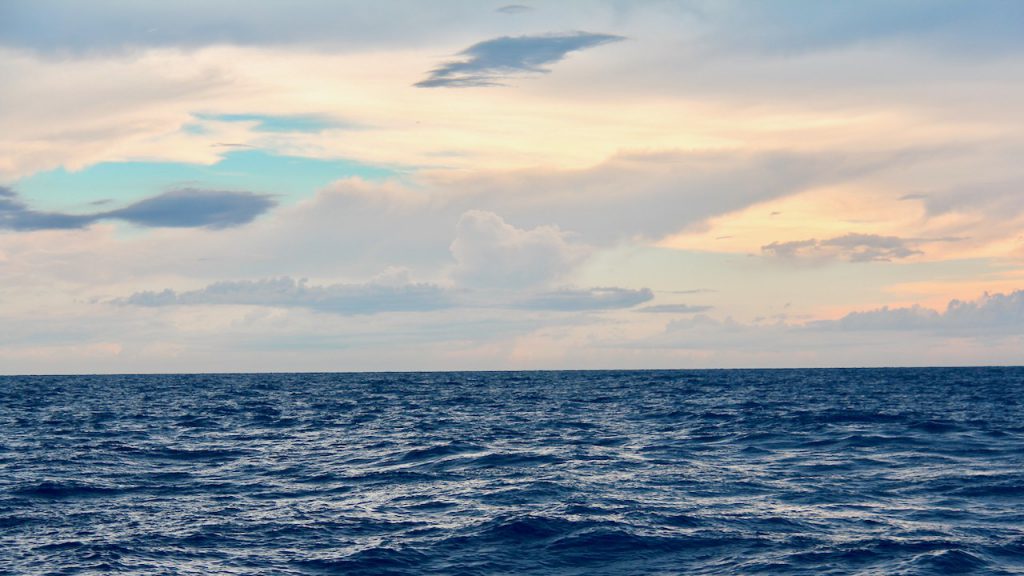 A photo shows a cloudy seascape and deep ocean waters. Photo Credit: NOAA AOML.