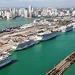 The Port of Miami with green water and a line of cruise ships (white) docked at the landing.