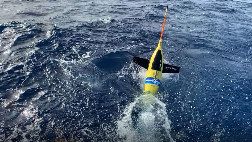 Half of a yellow underwater glider pops out of the ocean after deployment.