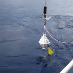 A white PIES lowered into the ocean off the side of a ship.