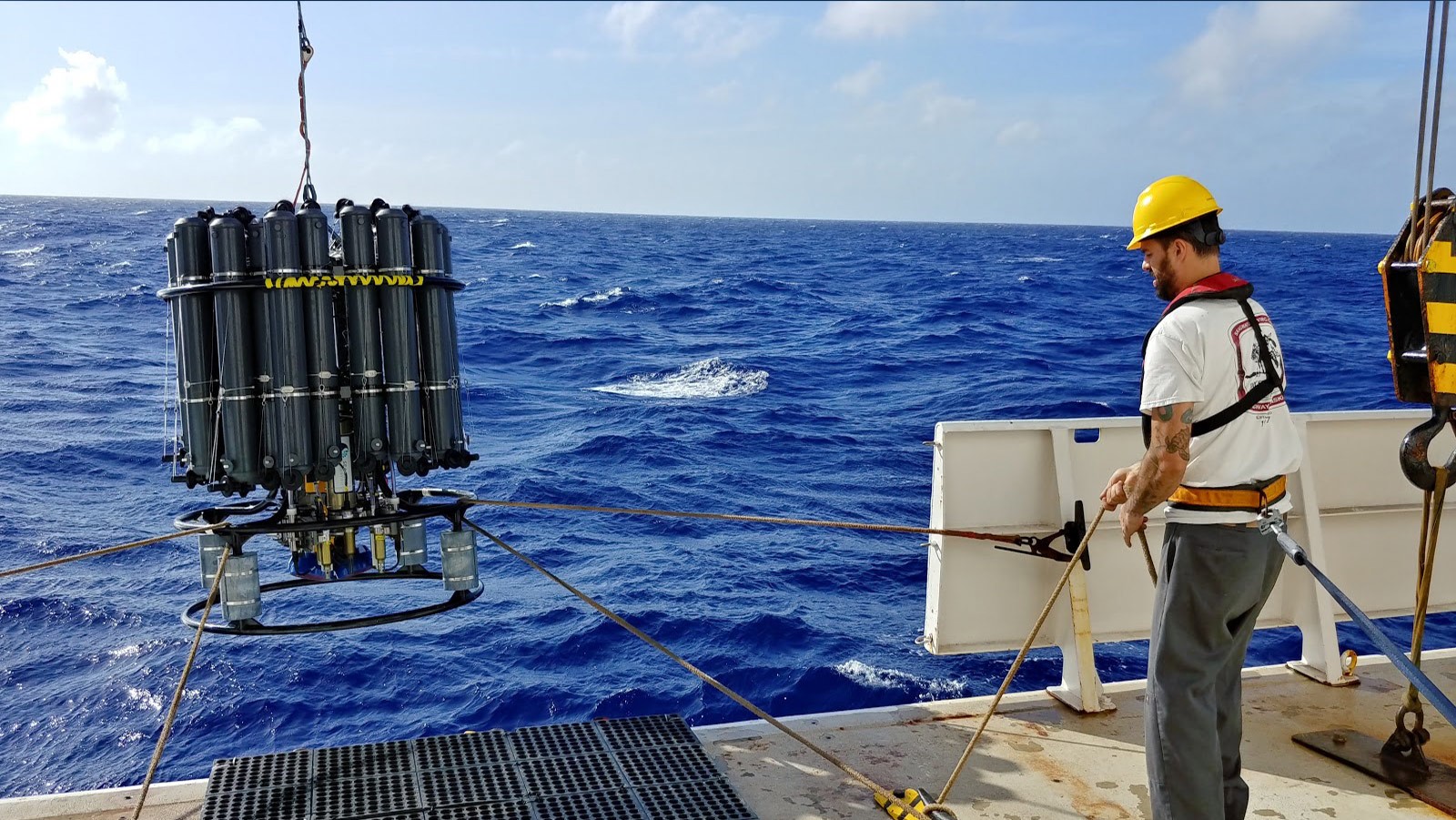 A large black CTD is deployed into the bright blue ocean. WBTS. Grant Rawson of AOML.
