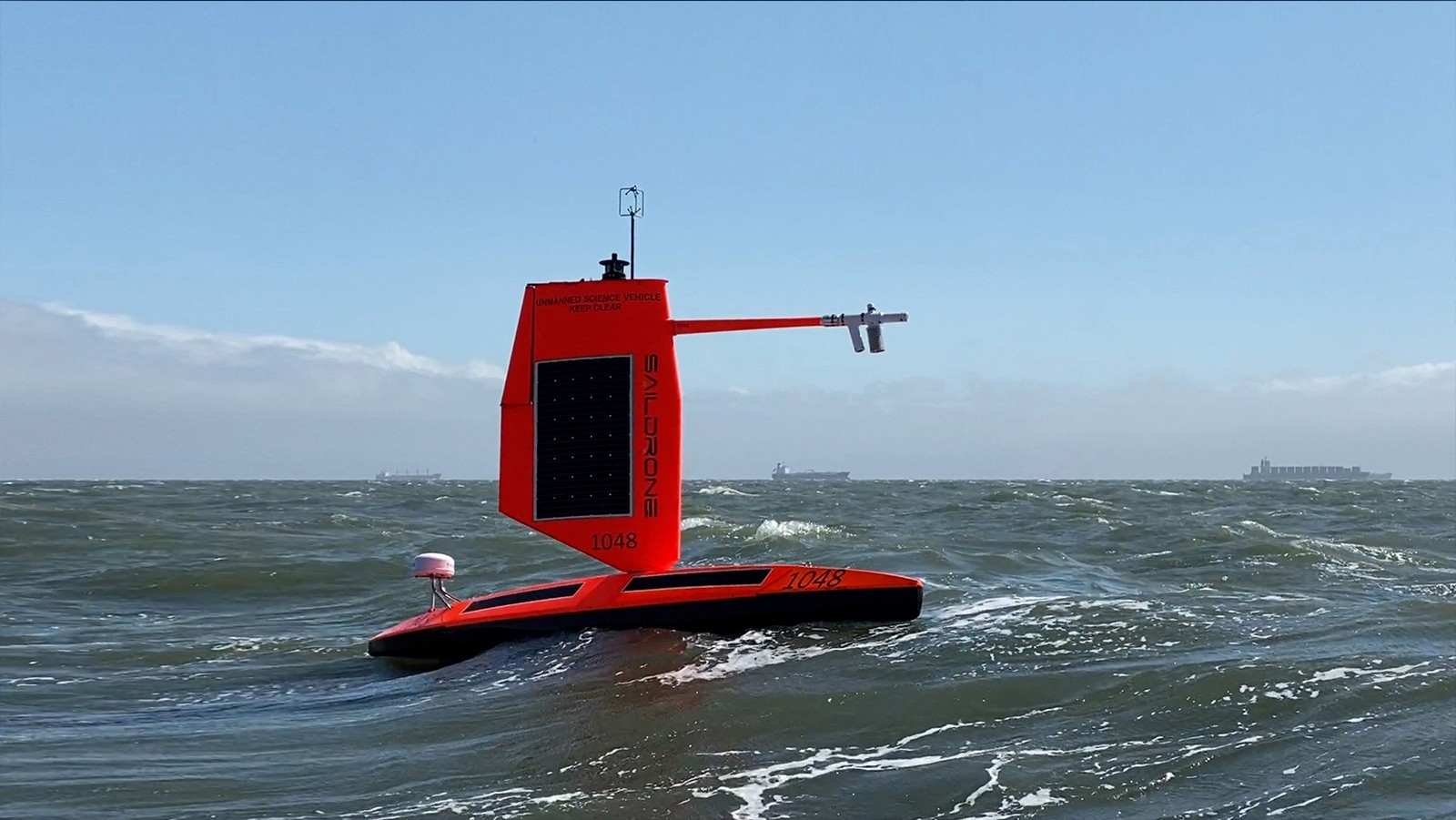 A large orange/red saildrone floats in the ocean