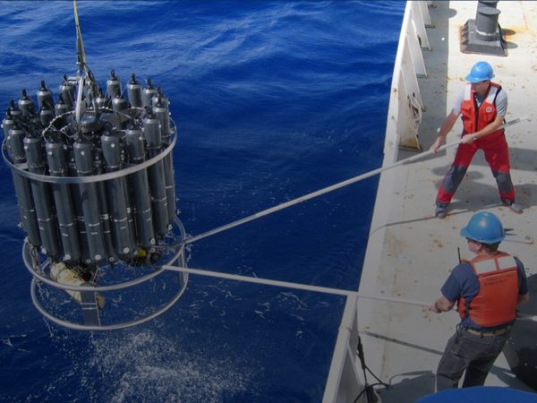 Two NOAA scientists deploy a large CTD into the ocean.
