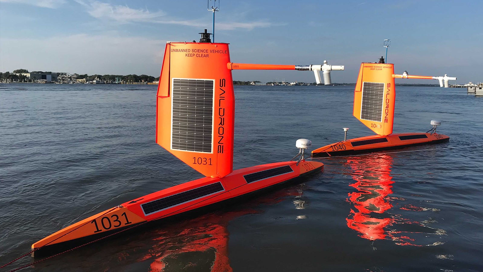 Two large orange saildrones in the calm ocean.