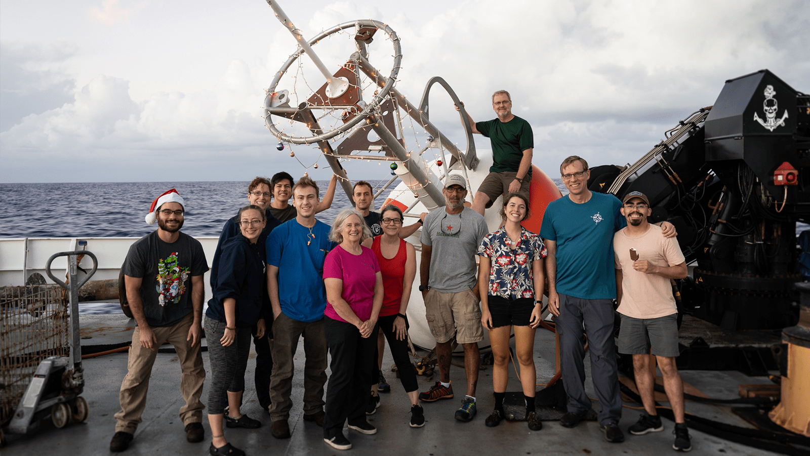 A PIRATA buoy is decorated with Christmas lights while the thirteen members of the PNE 21' cruise stand in front of it.