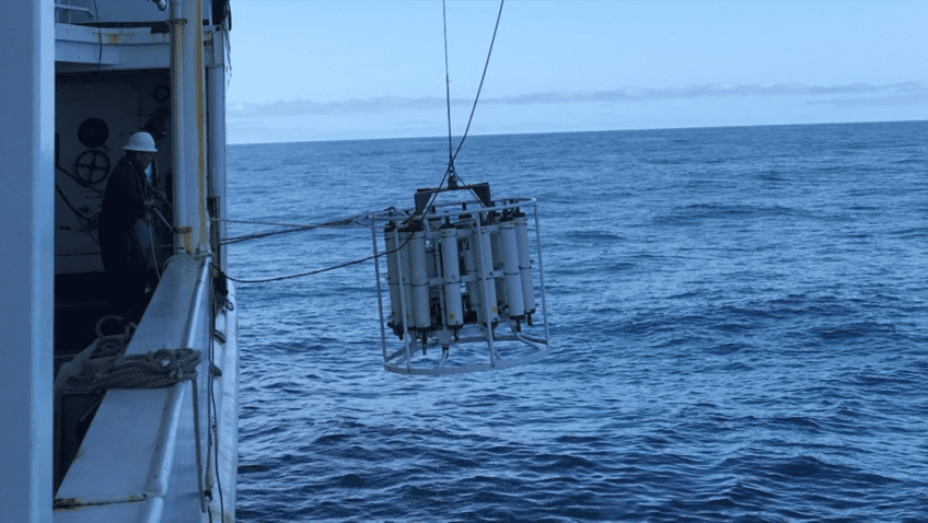 Un gran CTD blanco siendo desplegado en el océano por el lado de un costado.