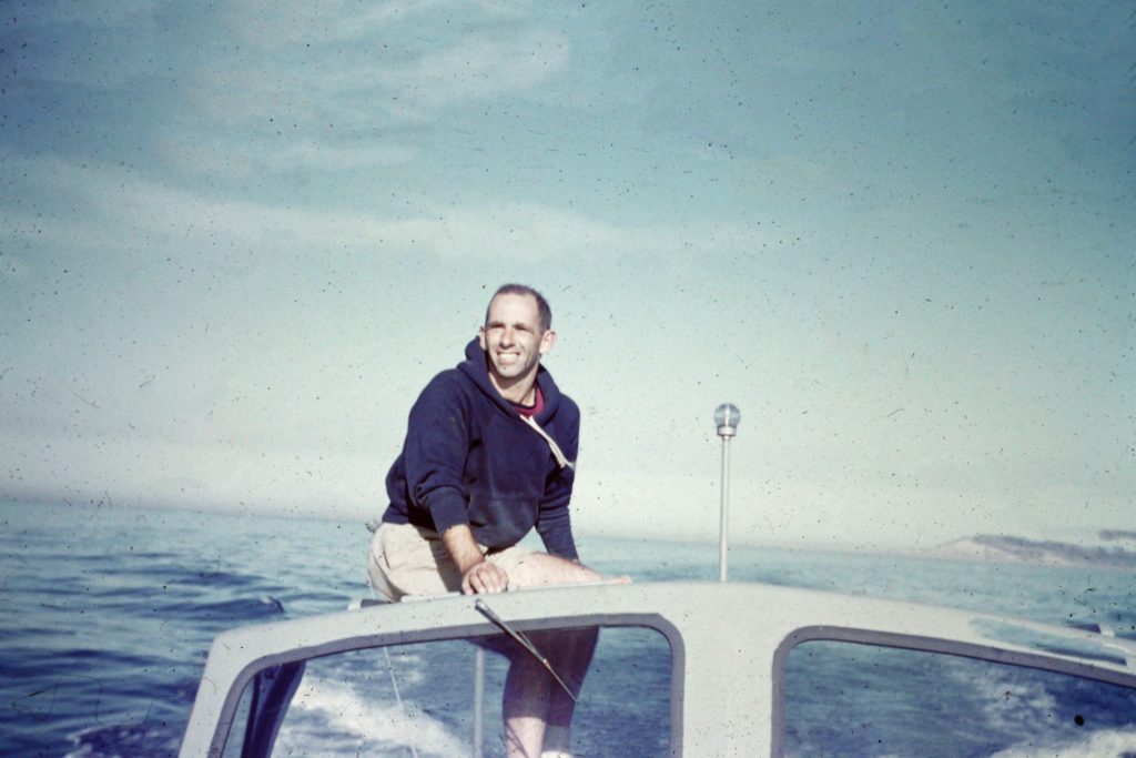 Colored image from AOML's Archive of AOML's first director Dr. Harris B. Stewart Jr. sitting on a boat while at sea. 