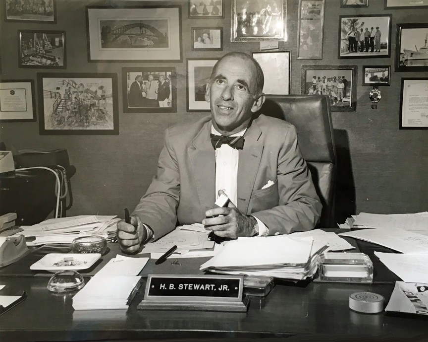 A black and white image from AOML's Archive of AOML's first director Dr. Harris B. Stewart Jr. sitting at his desk looking up toward the camera.