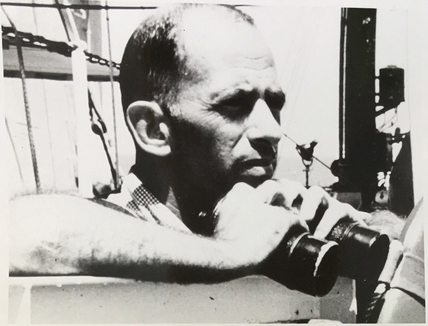 A Black and White image from AOML's Archive of AOML's first director Dr. Harris B. Stewart Jr. aboard a ship looking out at sea while holding binoculars.