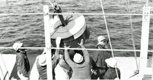 Five men release a floating scientific instrument off the side of a boat into the water