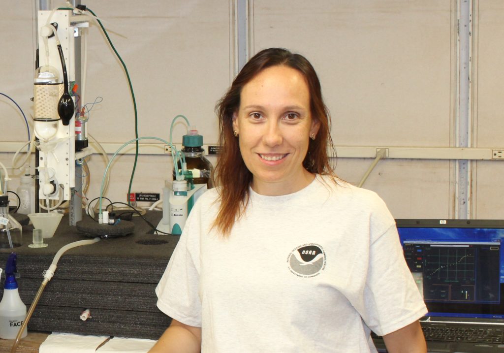 La Dra. Leticia Barbero, científica del AOML/CIMAS, sonríe con una camiseta de la NOAA en un laboratorio de investigación.Photo Credit: NOAA/AOML