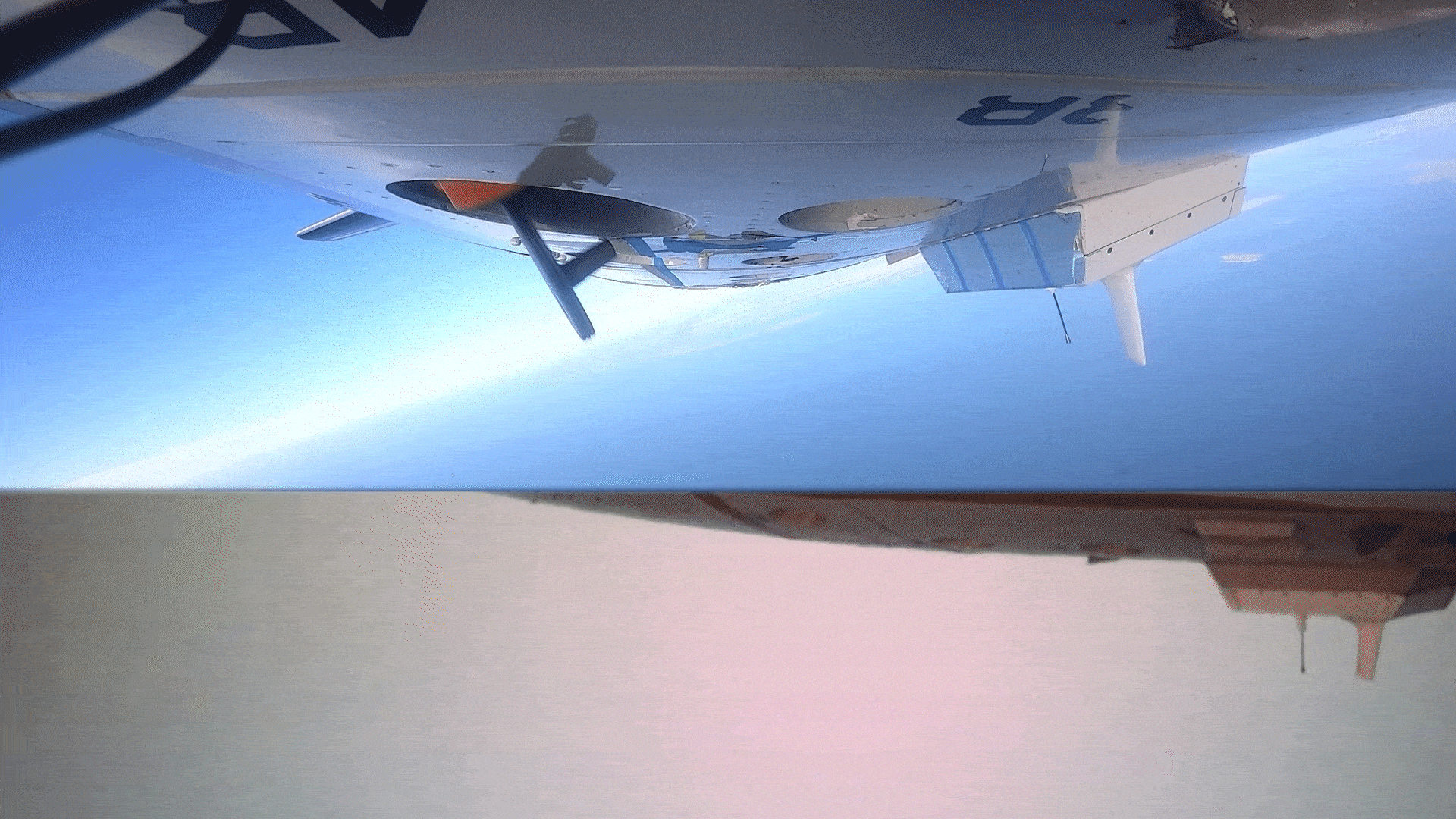 Animated gif that shows an Altius unmanned aircraft being released from the bottom of a p-3 aircraft. It is an orange cylinder with a black nose, released back first, as it exits the aircraft it rotates and two rear vanes extend before it leaves the bottom of the frame. The gif is split into top and bottom panes with the top portraying a front view, and the rear depicting a starboard view of the probe. These uncrewed sampling vehicles allow measurements closer to the sea surface increasing the ability of researchers to measure how heat in the ocean surface sustains a storm and improves intensity forecasts