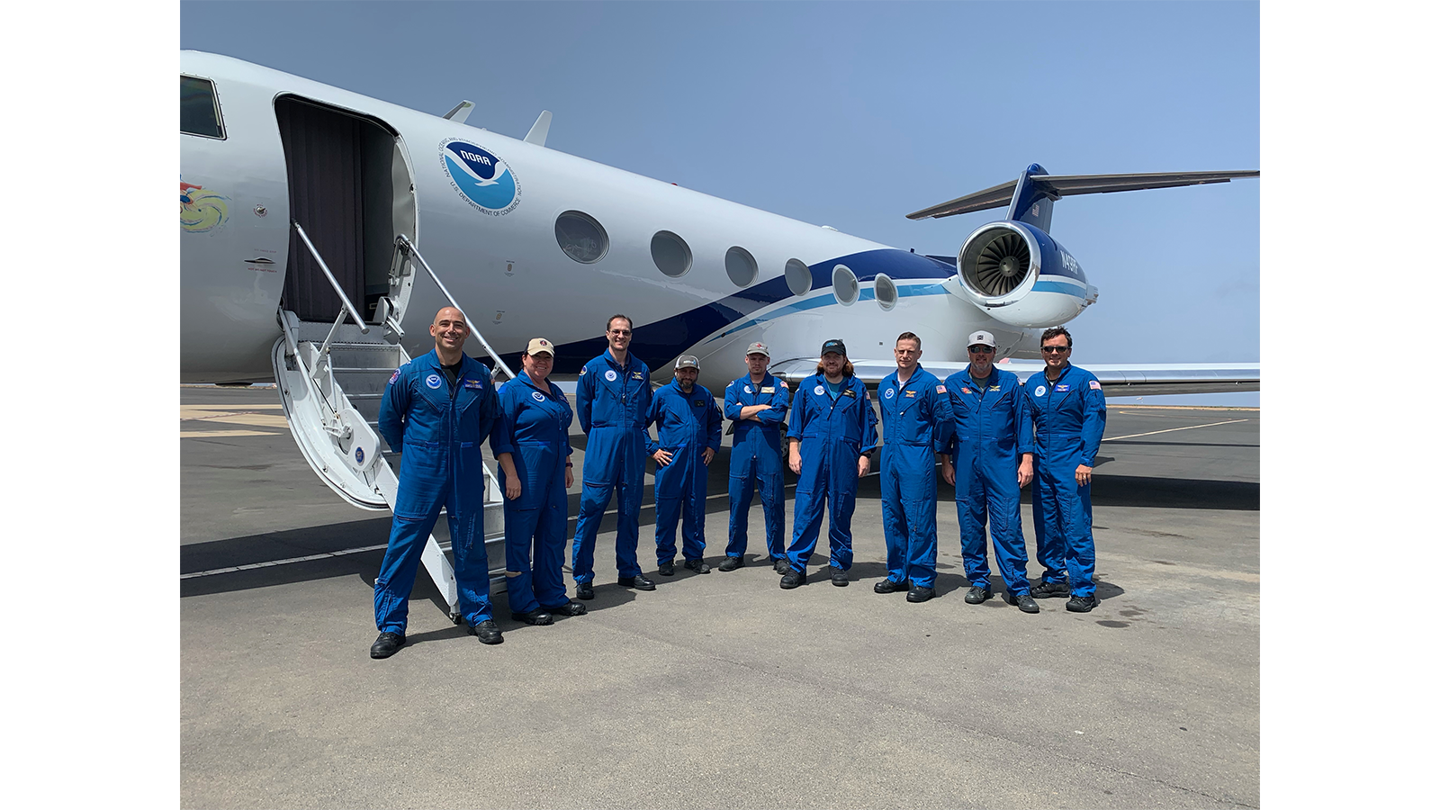 NOAA researchers, pilots, and crew in their blue flight suits stand in front of a NOAA G-IV Hurricane Hunter aircraft.
