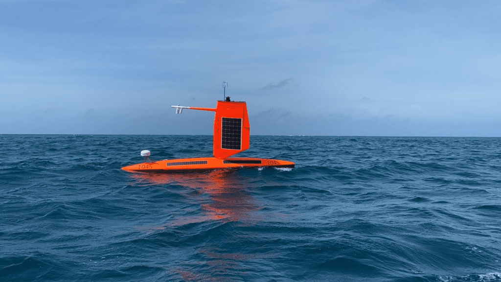 Fotografía en color que muestra un Saildrone naranja navegando en el Golfo de México. Este vehículo de superficie no tripulado permite realizar mejores mediciones de la interfaz superficie-aire, lo que mejora la precisión de las previsiones