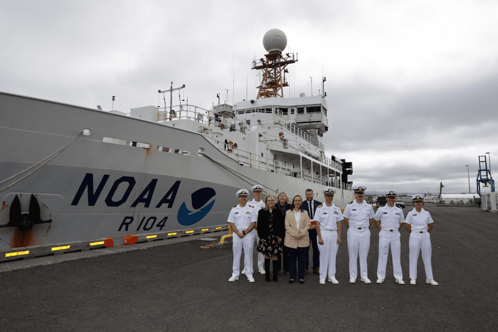 Diez personas frente al buque Ronald H. Brown de la NOAA. Oficiales del Cuerpo NOAA, científicos y embajadores.