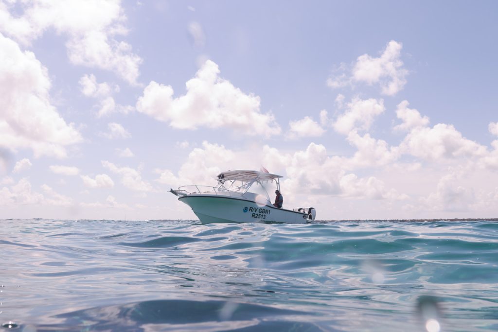 Marine vessel (white) floats above glassy blue water and beneath a blue sky with white clouds. 