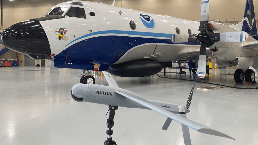 pequeño modelo gris de sistema de avión sin tripulación Altius en primer plano con el avión P-3 en segundo plano