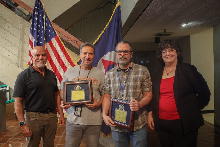 John Cortinas, Uli Rivera, Francis Bringas, Molly Baringer juntos delante de las banderas estadounidense y de la NOAA.