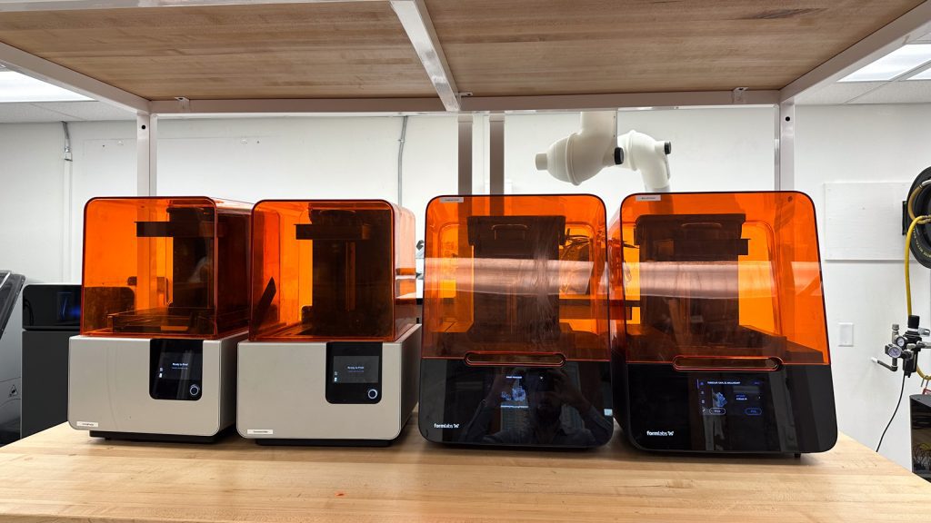 An image of three three-dimensional printers on a wooden shelf