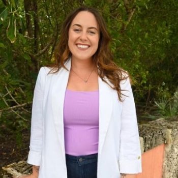 Bailey Morris in a white coat and a purple shirt with green trees behind her