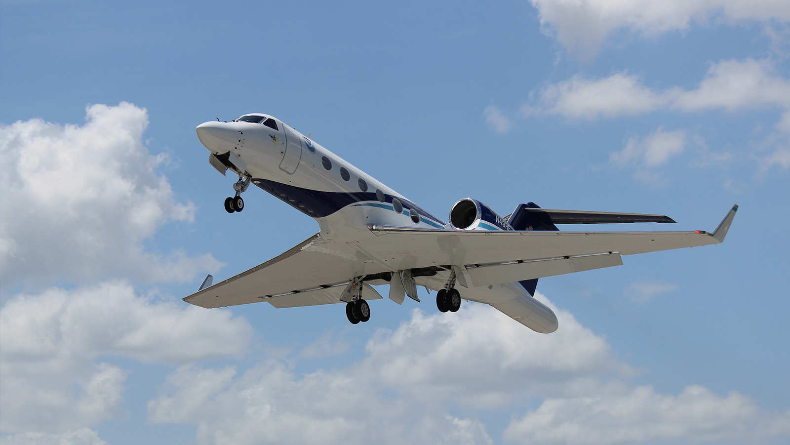 NOAA G-IV aircraft flying overhead with blue sky and clouds in the background